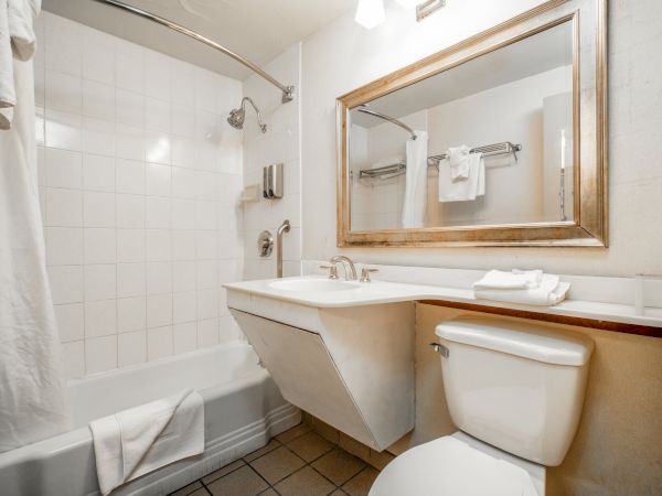 A bright hotel bathroom with a bathtub, showerhead, tiled walls, a sink, toilet, and neatly folded white towels.